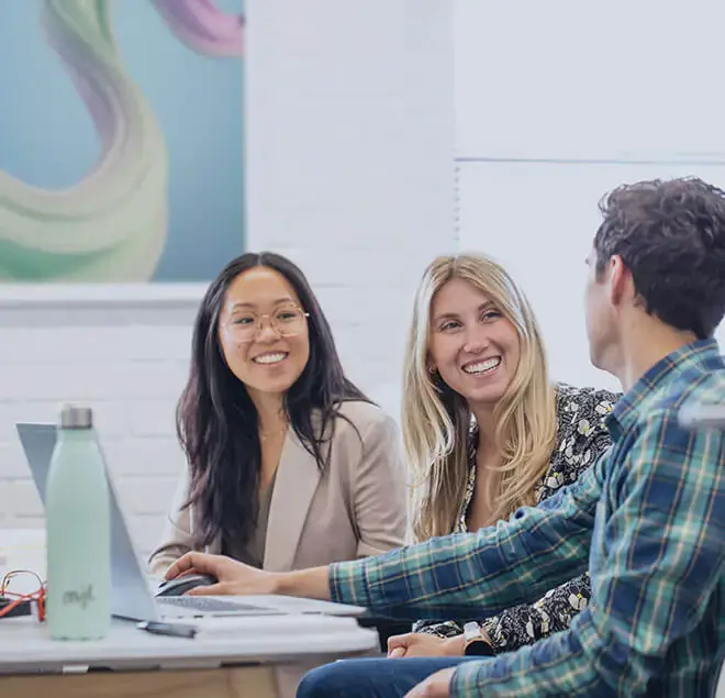 Three people sat at a desk laughing and having fun at work