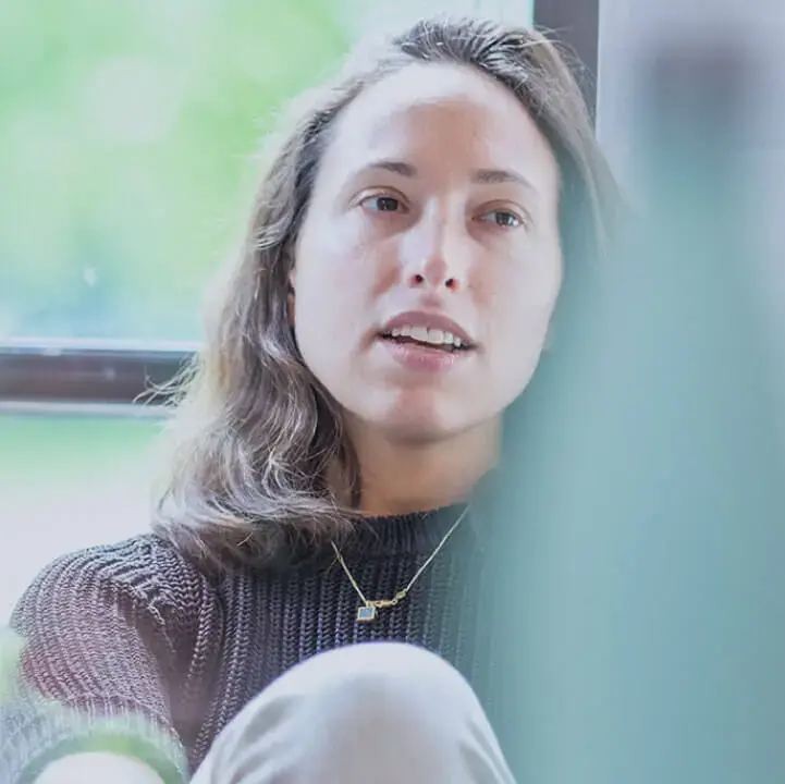 A person sitting thoughtfully by a window, with some blurry and colourful drinks bottles in the foreground